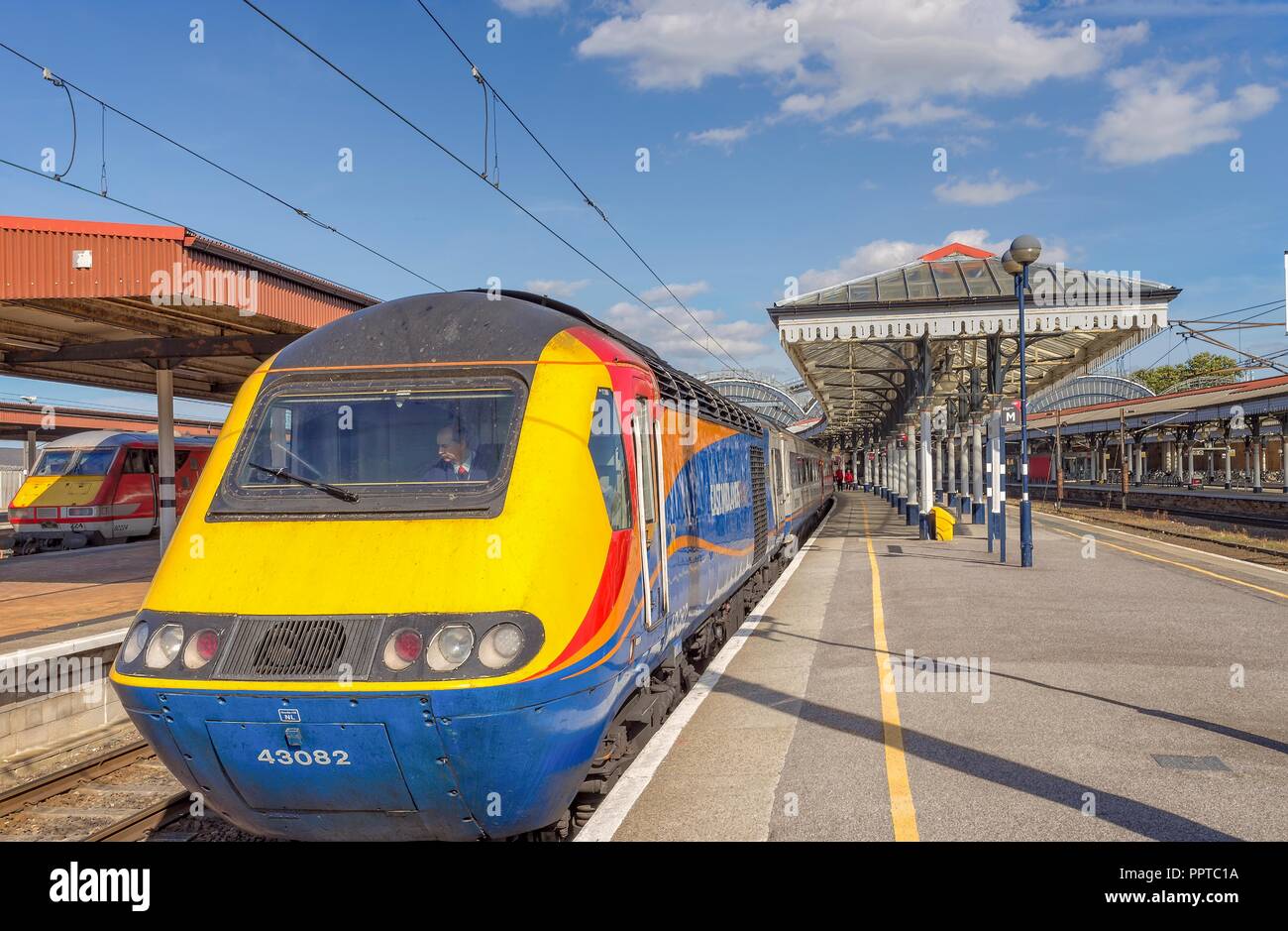 Vista tipica di un treno si preparano a partire a una stazione ferroviaria piattaforma. Un edificio del XIX secolo la tettoia è su di un lato e un cielo blu è sopra. Foto Stock