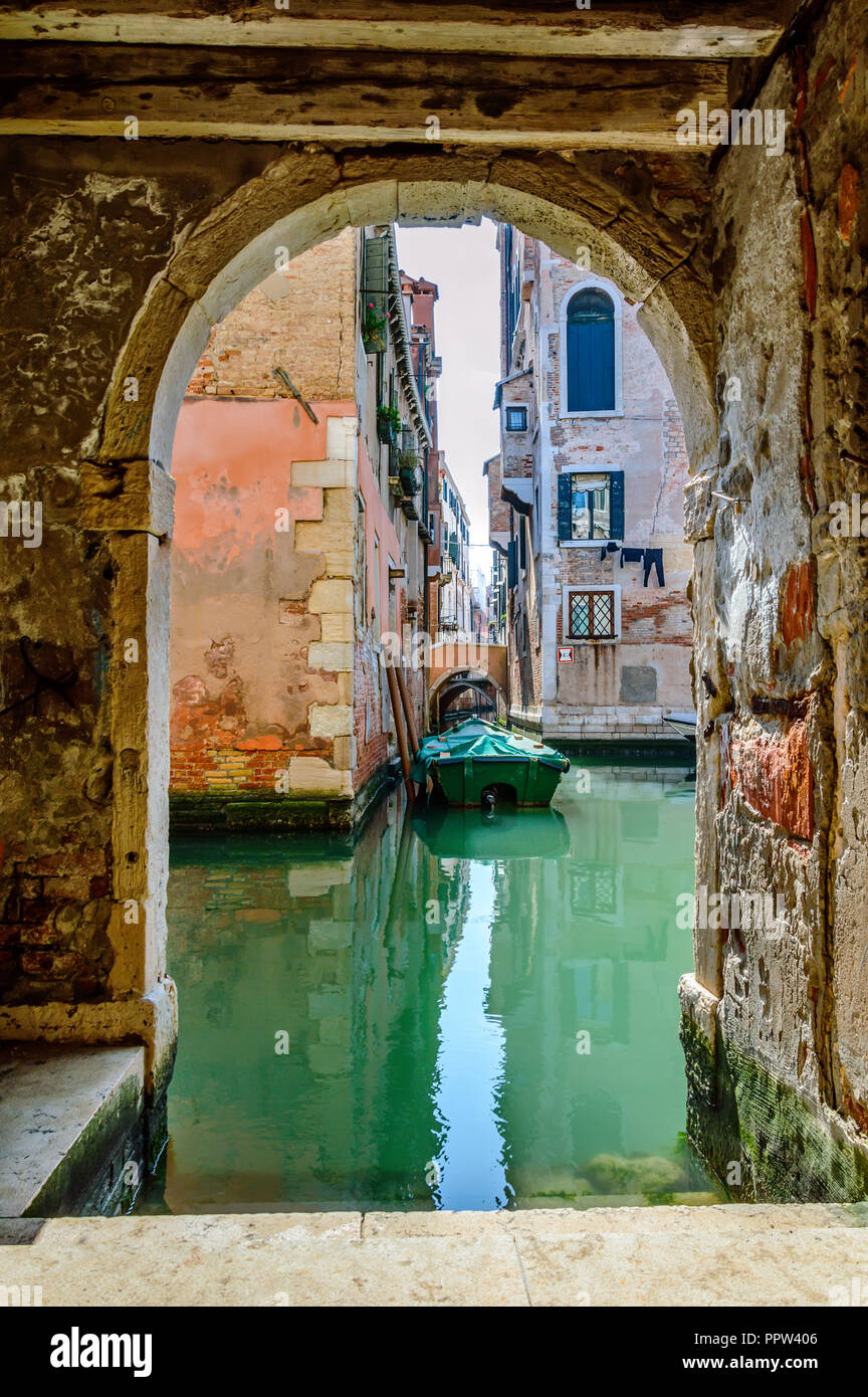 Venezia, Italia: scenic canale veneziano con acqua verde e una barca, vista da un arco Foto Stock