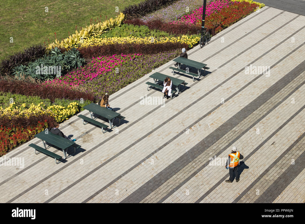 Scena urbana con il lavoratore edile e la gente seduta al pik-nik tabelle in città. Il paesaggio urbano - fiori piante ans in estate. Bike attaccato ad un Foto Stock