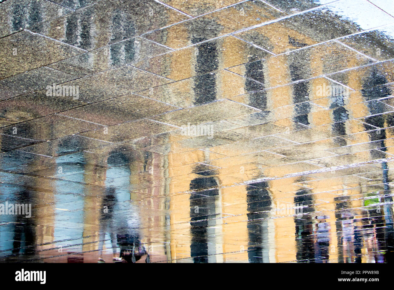 Sfocata riflessione silhouette di ombra in una pozza delle persone che camminano sulla città piovosa street Foto Stock