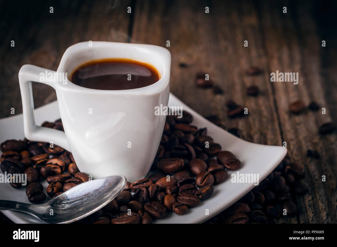 Un quadrato tazza di caffè sul vecchio tavolo in legno con fumo, alcuni grani un cucchiaio Foto Stock