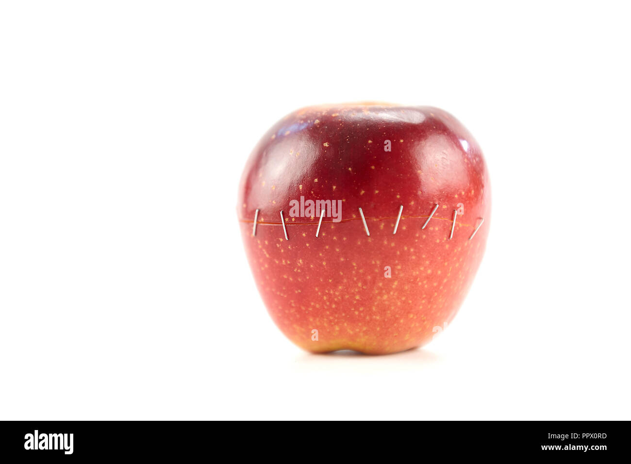 Due metà di una mela rossa tenuti insieme mediante punti metallici isolati su sfondo bianco. Foto Stock