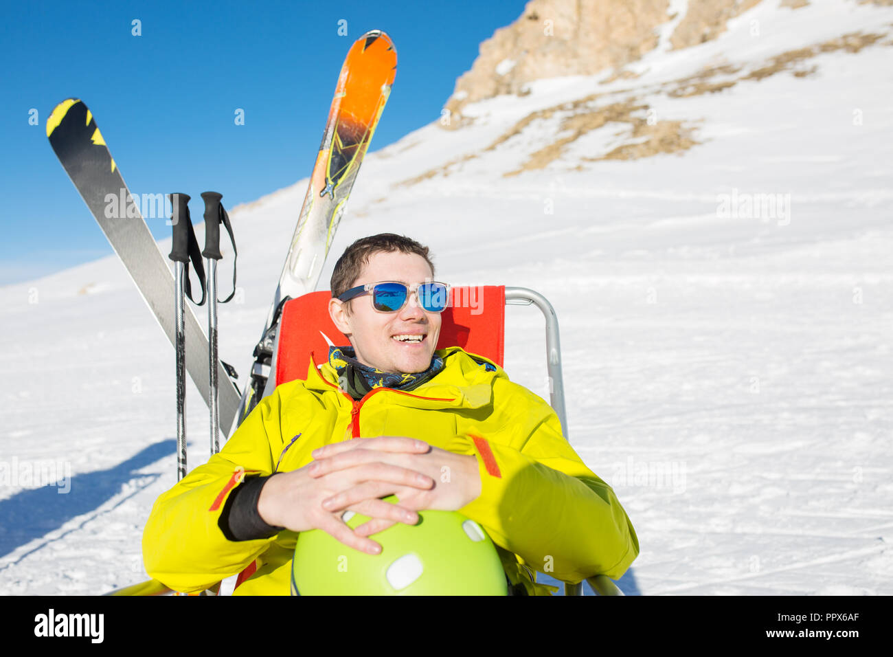 Immagine di sport uomo seduto sulla sedia accanto a sci e bastoni sullo sfondo di montagne innevate Foto Stock
