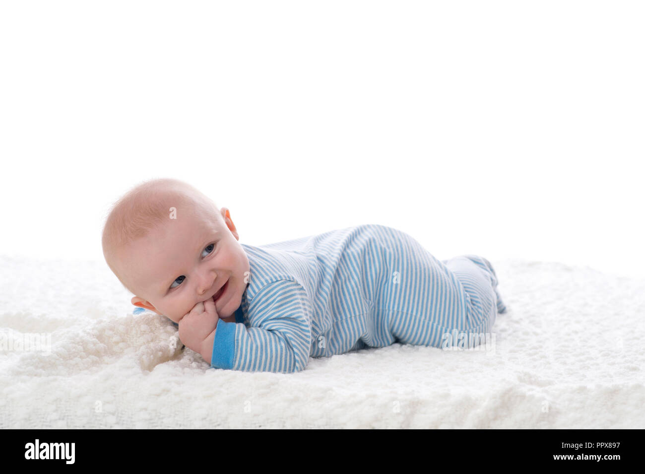 A 2 mesi di età Bimbo giacente sul suo stomaco su una coltre bianca. Egli indossa il pigiama, ha le sue dita nella sua bocca e ha un sorriso malizioso. Girato e mi Foto Stock