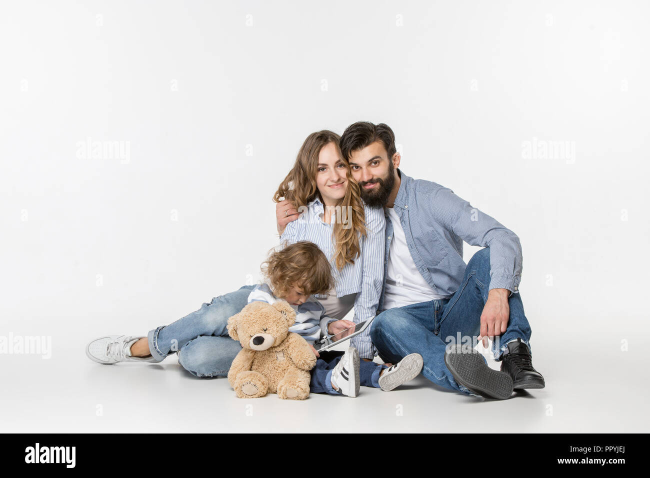 Famiglia sorridente seduti insieme al bianco studio e guardare i loro cartoni preferiti sul computer portatile. Foto Stock