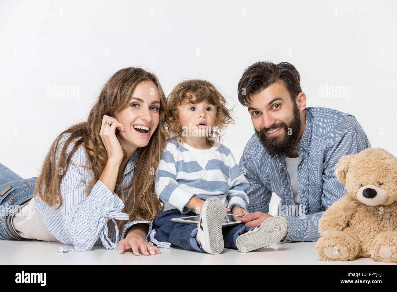 Famiglia sorridente seduti insieme al bianco studio e guardare i loro cartoni preferiti sul computer portatile. Foto Stock