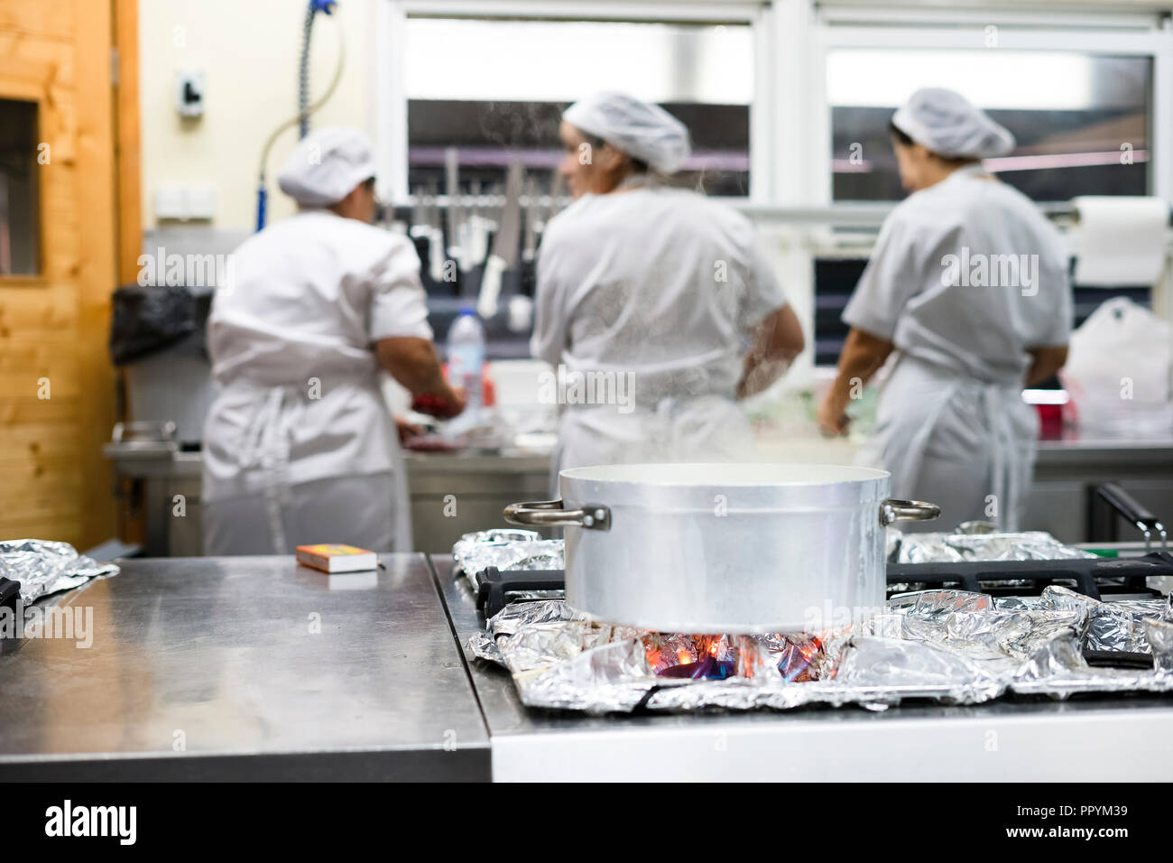 Cottura a vapore pentola in argento con tre lavoratori cucina indossando grembiuli come sfondo Foto Stock
