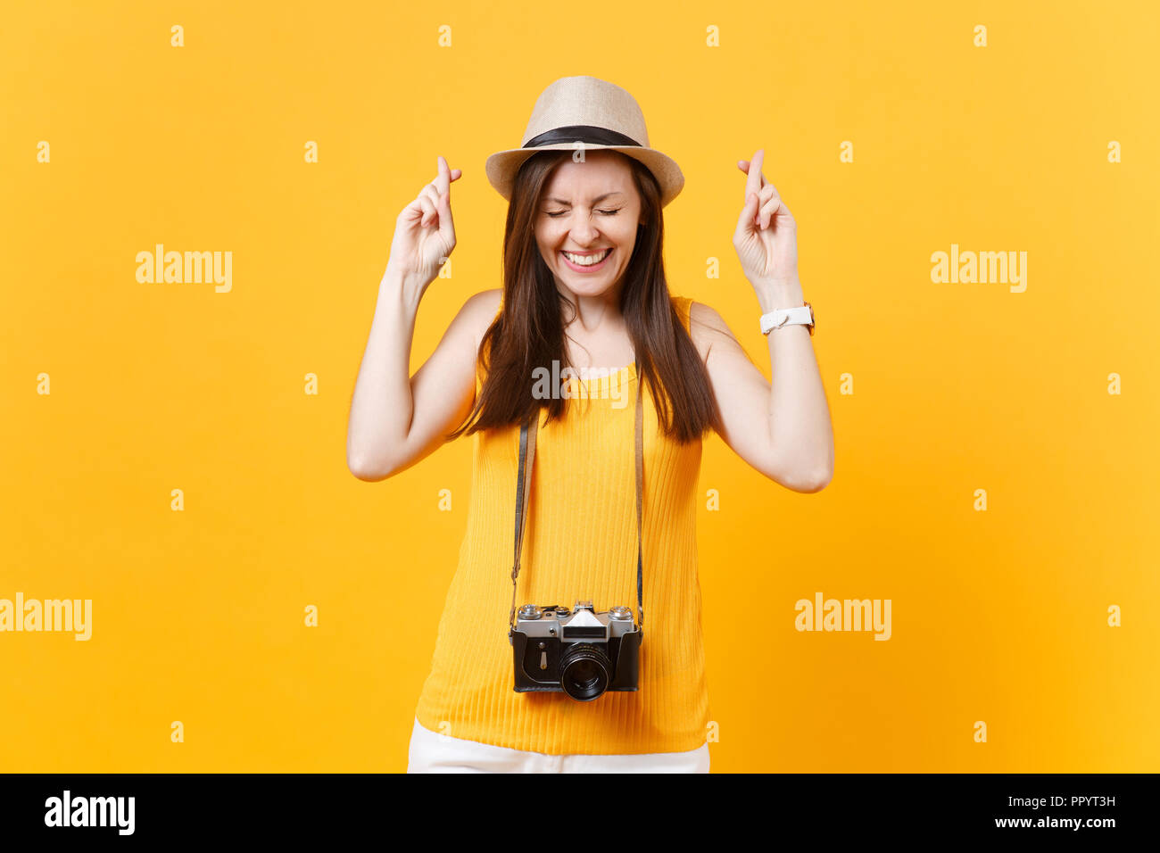 Donna turistica in estate abiti casual hat tenere le dita incrociate a occhi chiusi isolati su sfondo giallo. Femmina passeggero viaggia all'estero a trave Foto Stock