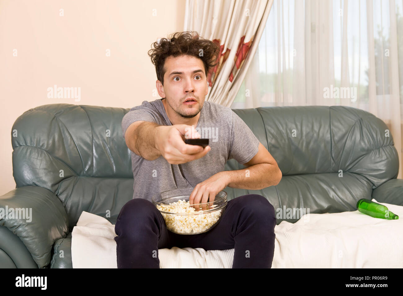 Eccitato giovane con il telecomando e popcorn sul divano guardando la tv Foto Stock