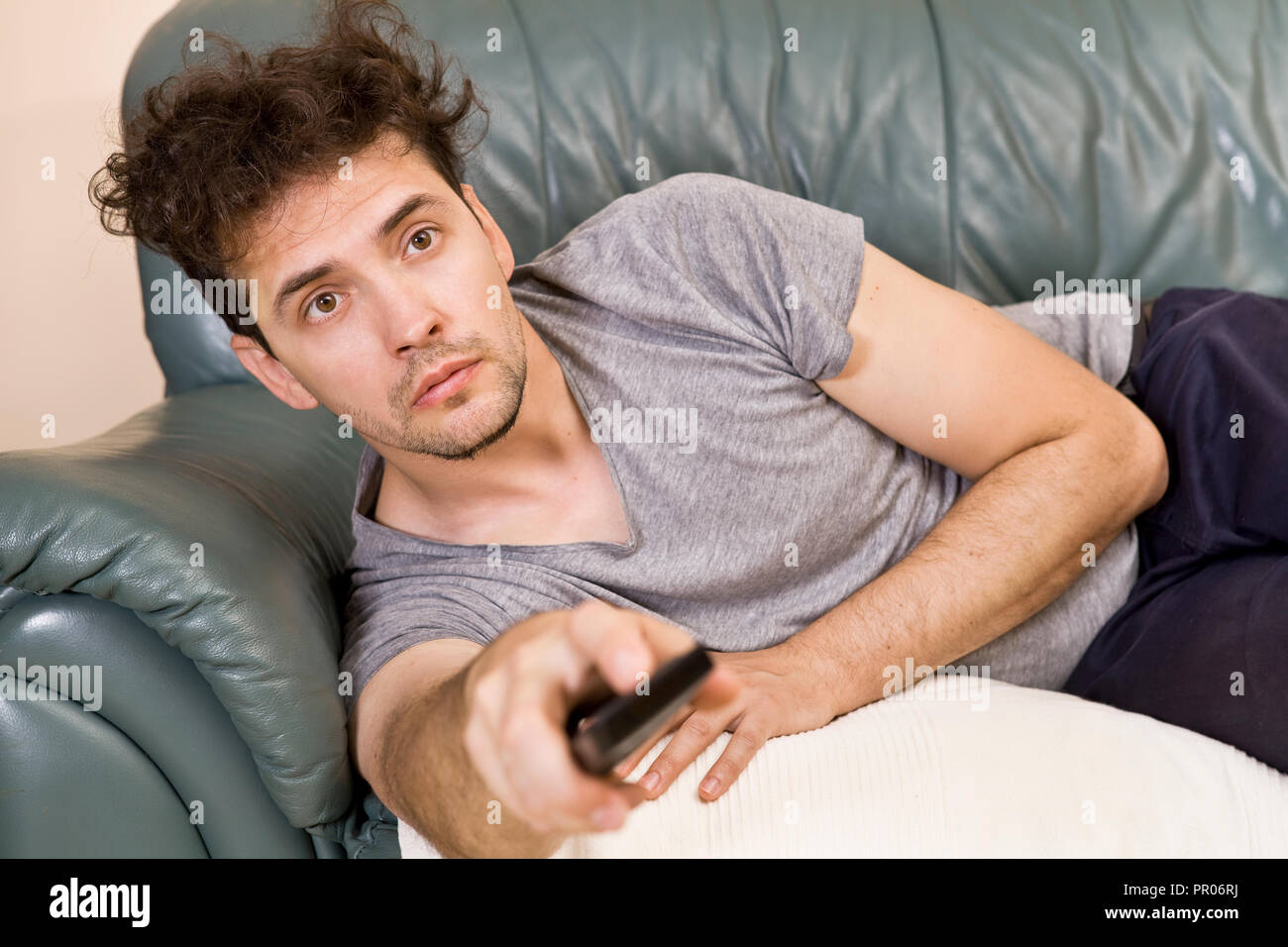 Un giovane uomo guarda la televisione e cambia i canali durante i momenti di relax Foto Stock