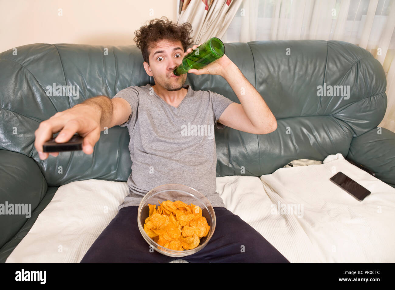Un giovane uomo guarda la televisione e cambia i canali durante i momenti di relax Foto Stock