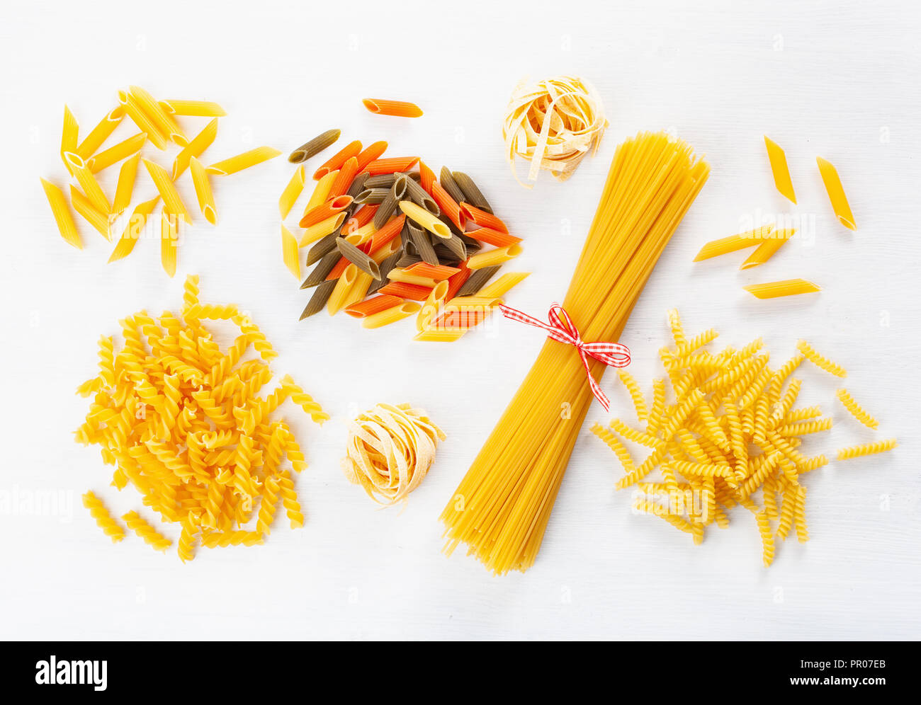 Un assortimento di pasta cruda laici piatta sul bianco. spaghetti fusilli penne tagliatelle girandole Foto Stock