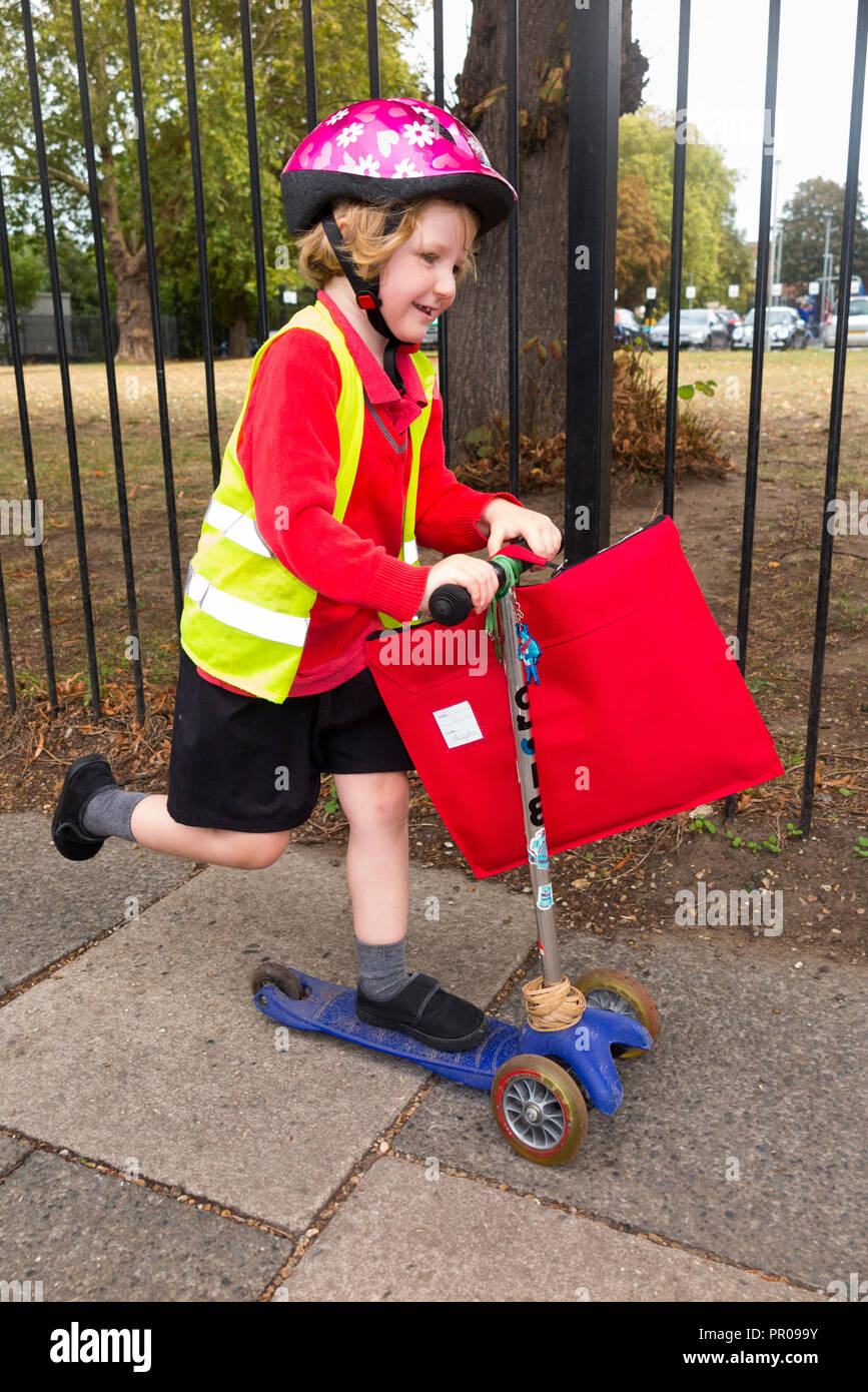 Bambino di 4 anni su scooter / ragazza la hi vis / alta visibilità giacca giubbotto di scooter a casa dalla scuola di classe di ricezione. Regno Unito. (102) Foto Stock