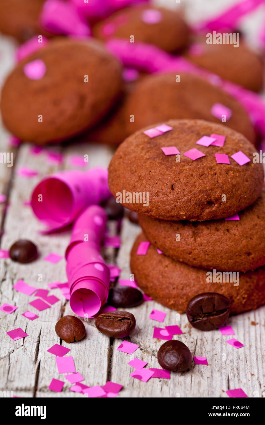 Fresco biscotti al cioccolato, i chicchi di caffè, rosa nastri e confetti sul rustico sfondo di legno Foto Stock