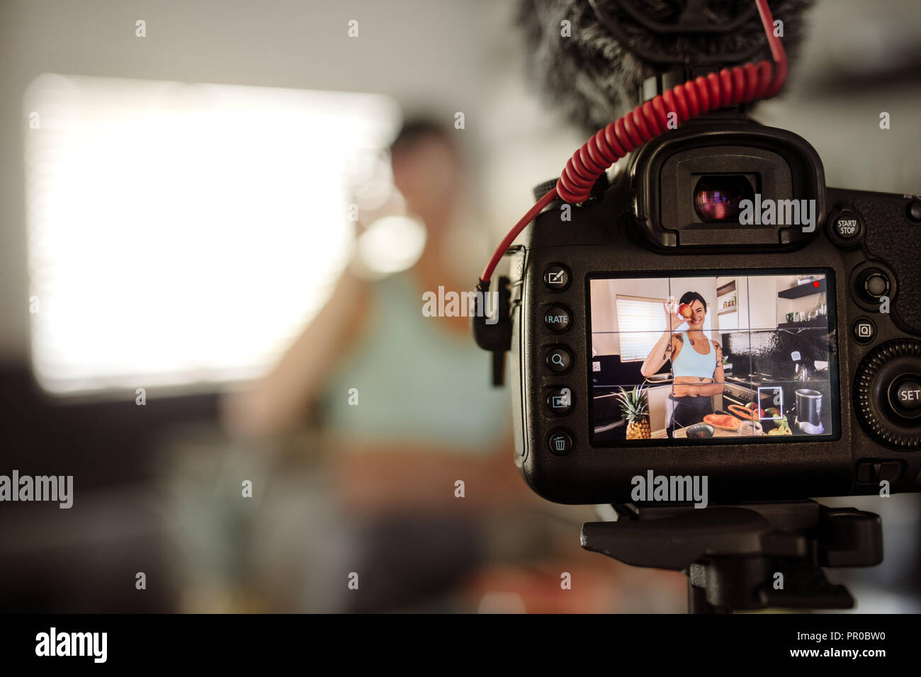 Lo schermo della fotocamera che mostra la donna tenendo un frutti nella parte anteriore del suo occhio in cucina. Donna che fa un video per il suo blog su mangiare sano. Foto Stock