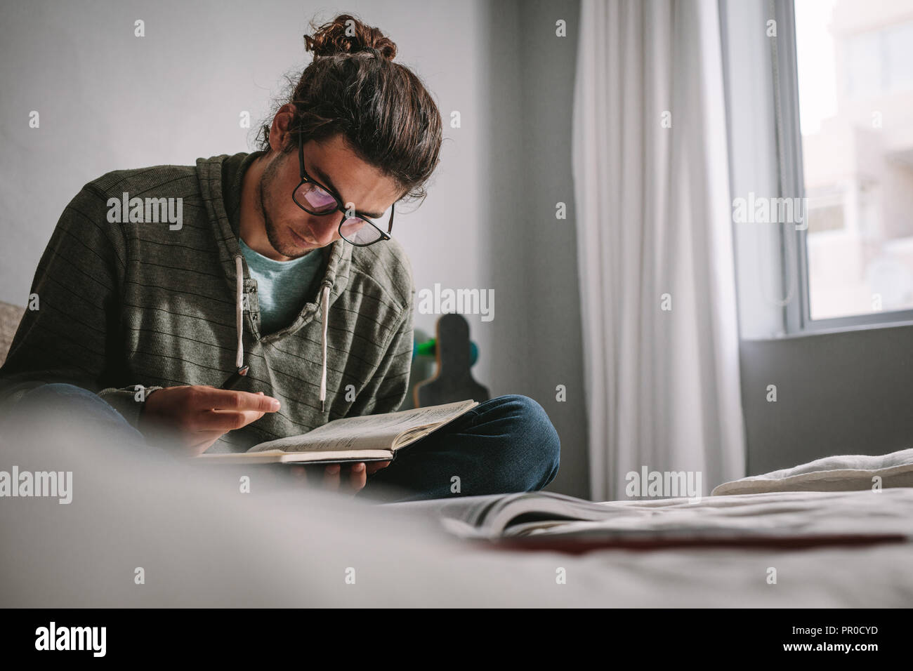 Studente studiando per gli esami seduti a casa. Giovane uomo la lettura di libri con concentrazione la preparazione per gli esami. Foto Stock