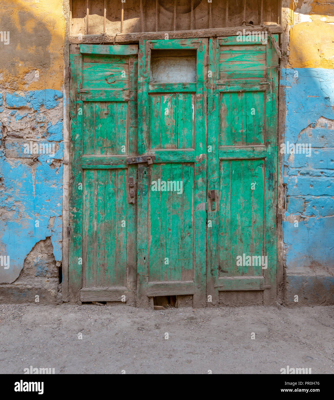 Chiuso in legno verde grunge weathered abbandonato porta sul muro sporco dipinte in giallo e blu Foto Stock