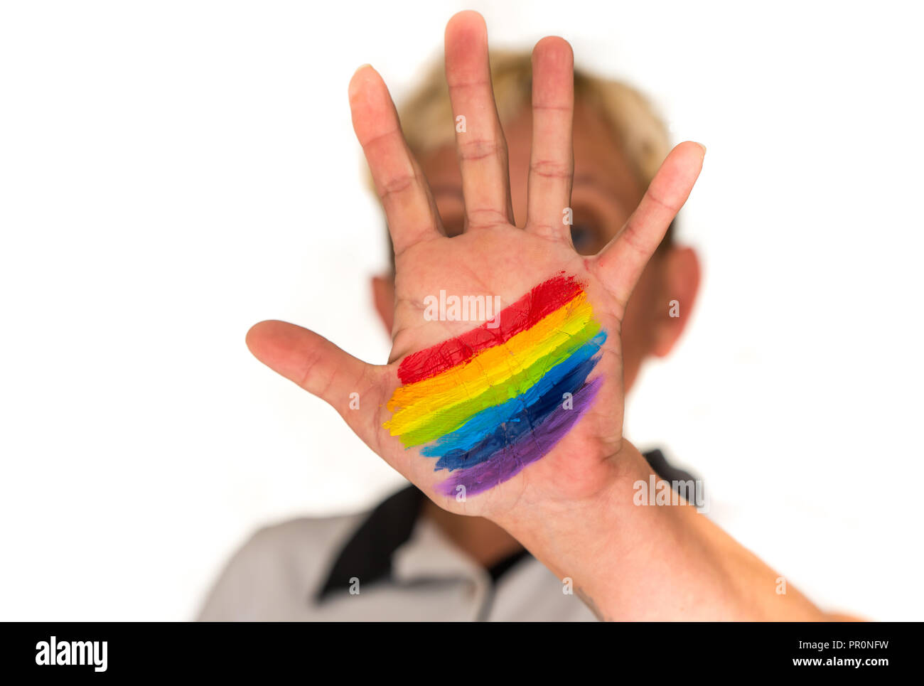 Una donna con corti capelli biondi, offuscata in uno sfondo luminoso, mostra la sua mano con un dipinto di Rainbow Foto Stock