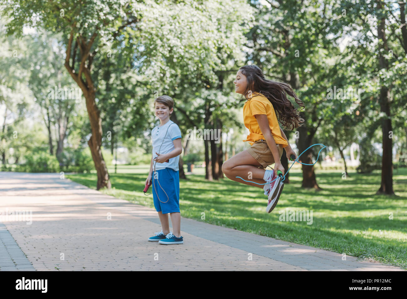 Adorabili bambini felici giocando e saltando con funi di salto in posizione di parcheggio Foto Stock