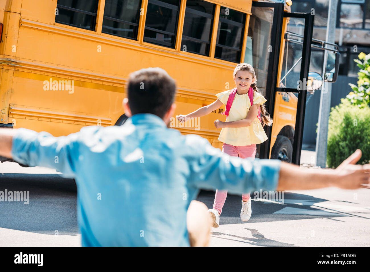 Padre con le braccia aperte in attesa per la figlia mentre era in esecuzione dal bus di scuola Foto Stock