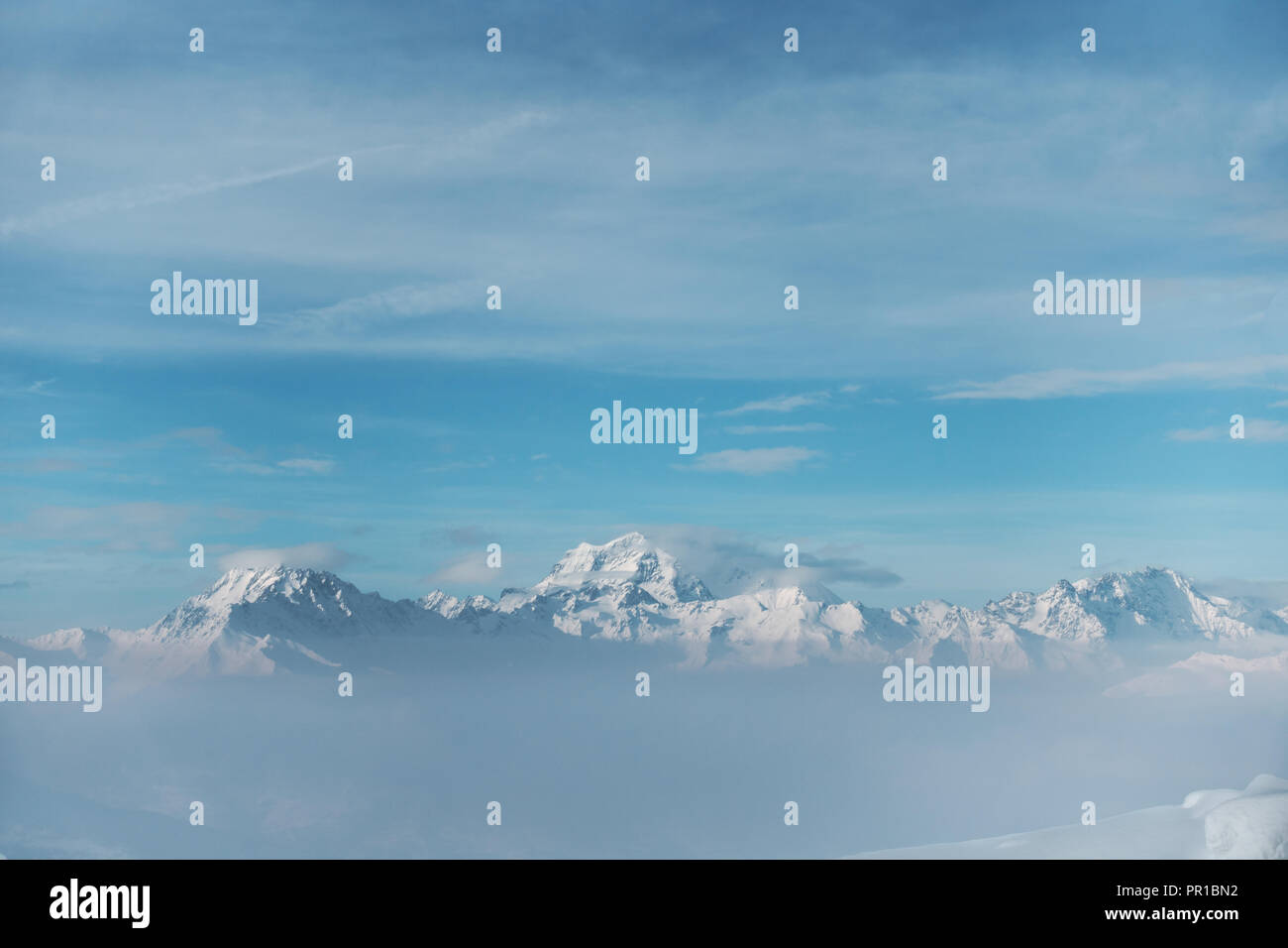 Montagna innevata gamma in una distanza, con nuvole sopra e sotto le cime, nebbia con un cielo blu Foto Stock