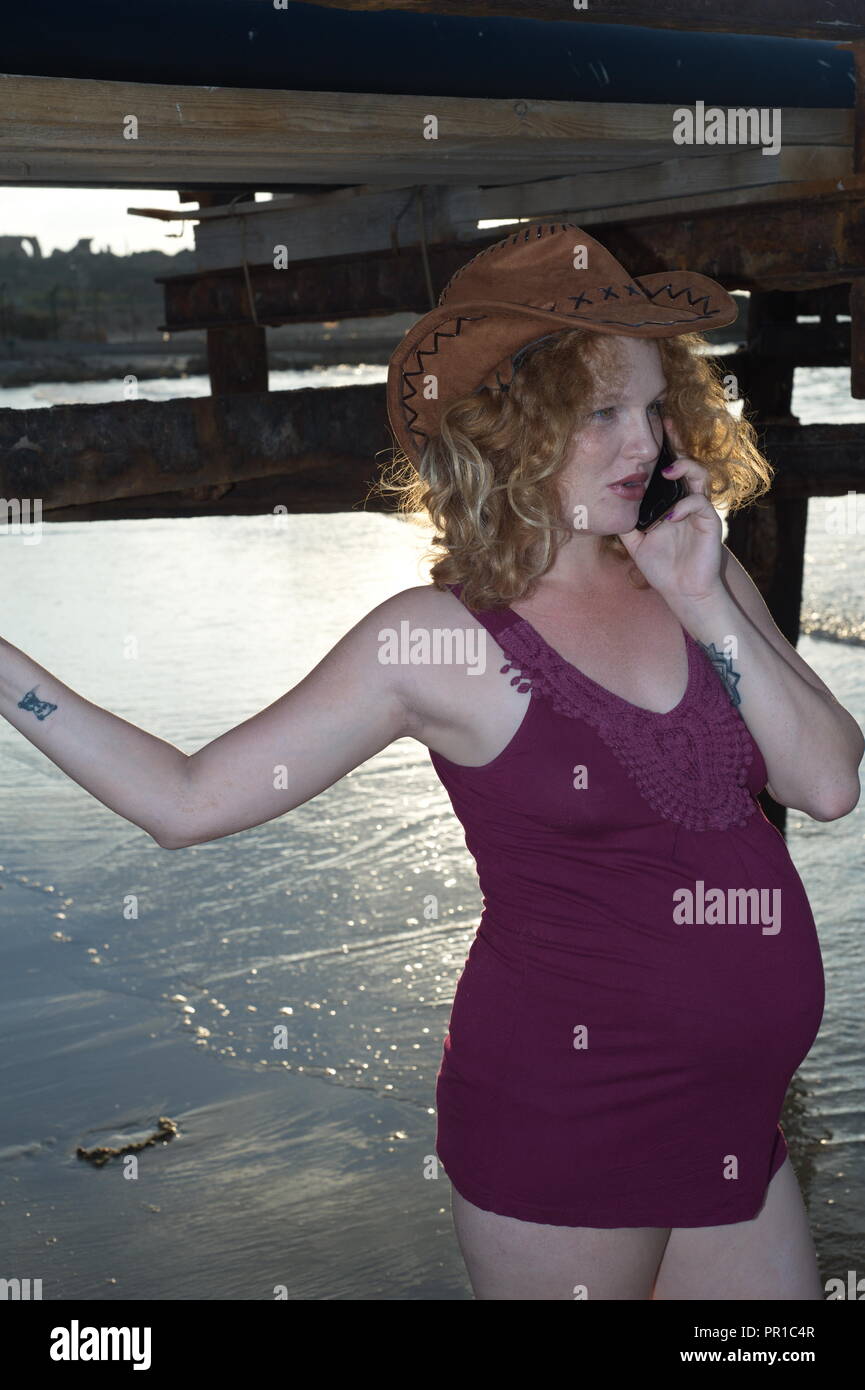 Redhead gravidanza lady parla con il cellulare sul mare costiero Foto Stock