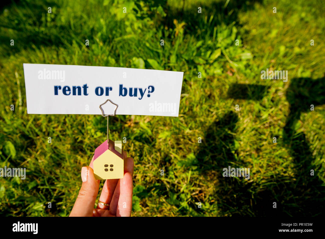 La questione di acquistare o noleggiare,scritto su un pezzo di carta rigata e modello di casa in mano femminile. Una decisione aiutata da analisi di mercato immobiliare e le nostre personali finanze.immobiliare di concetto. Foto Stock