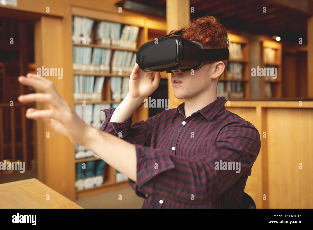 Studente di College utilizzando la realtà virtuale auricolare in biblioteca Foto Stock