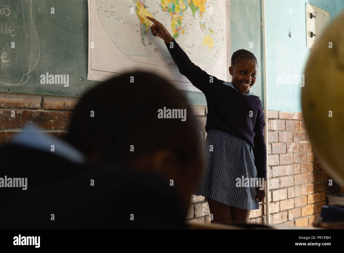 Schoolgirl spiegando sulla mappa del mondo in classe Foto Stock