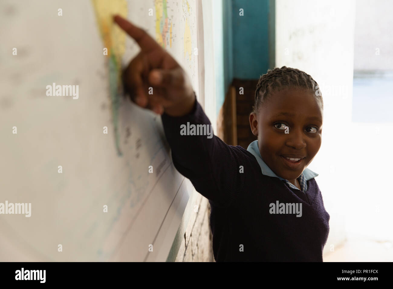 Schoolgirl spiegando sulla mappa del mondo in classe Foto Stock