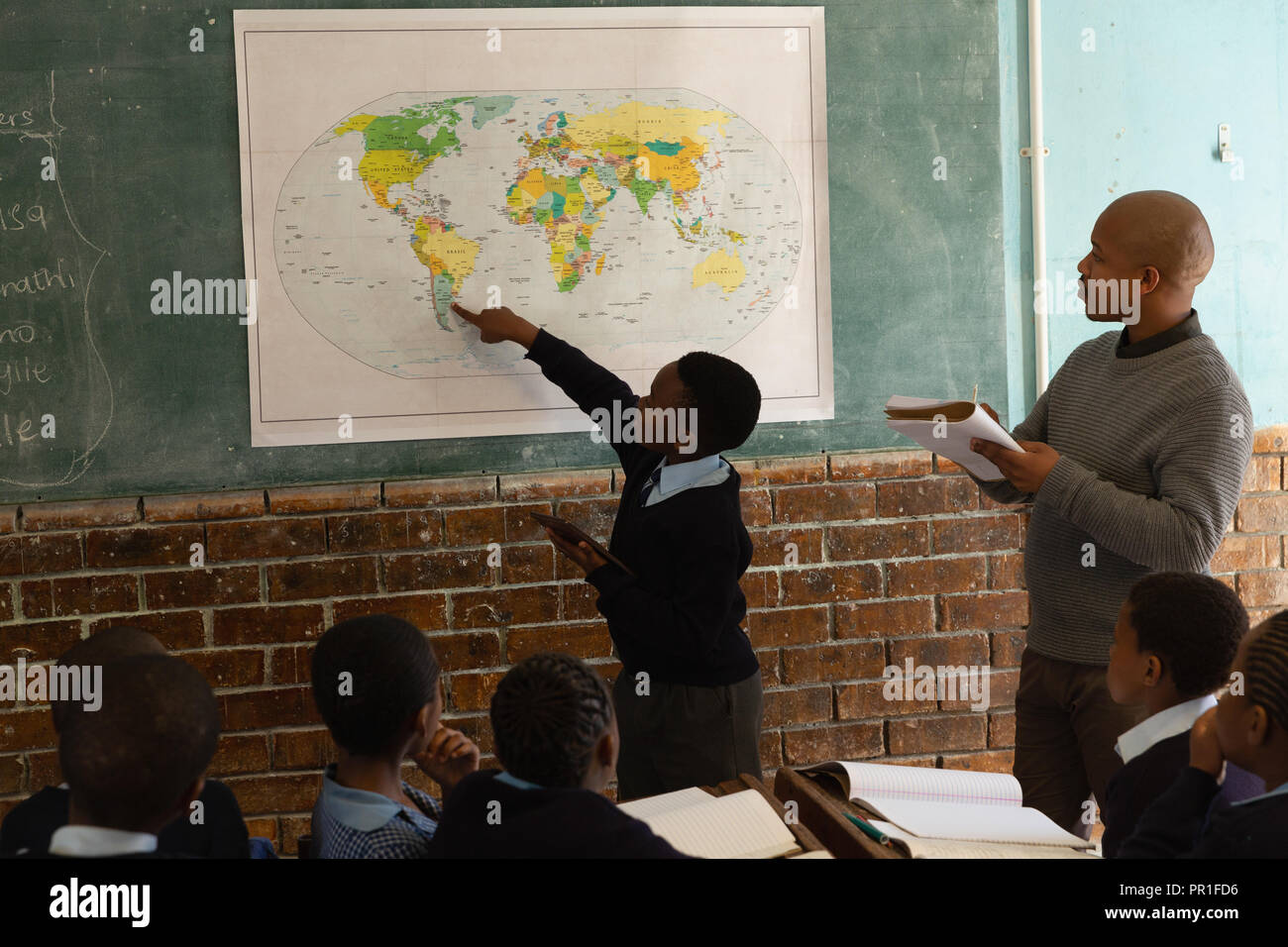 Scolaro spiegando sulla mappa del mondo in classe Foto Stock
