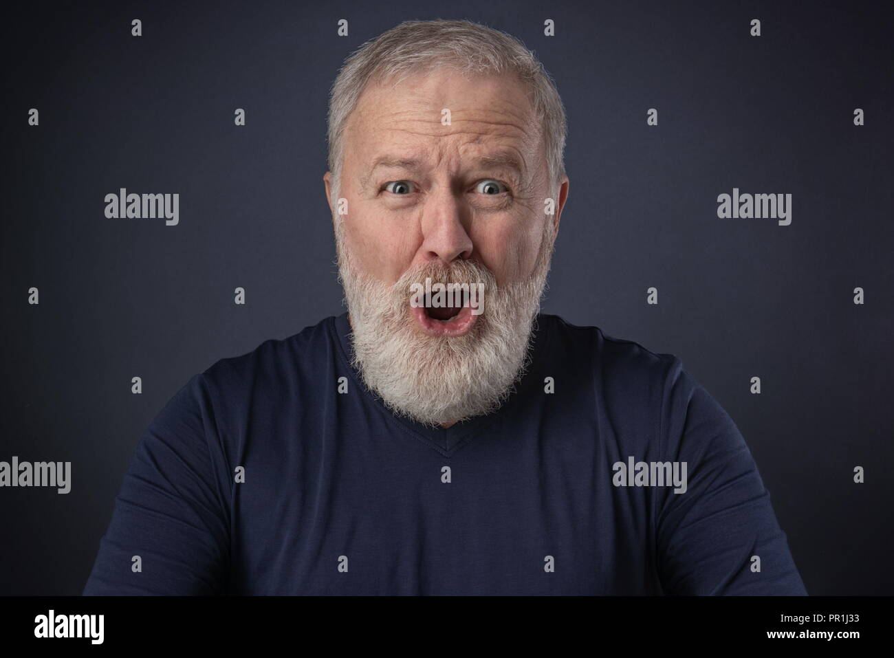 Un uomo anziano con una barba grigia con un molto sorpreso di imitare Foto Stock