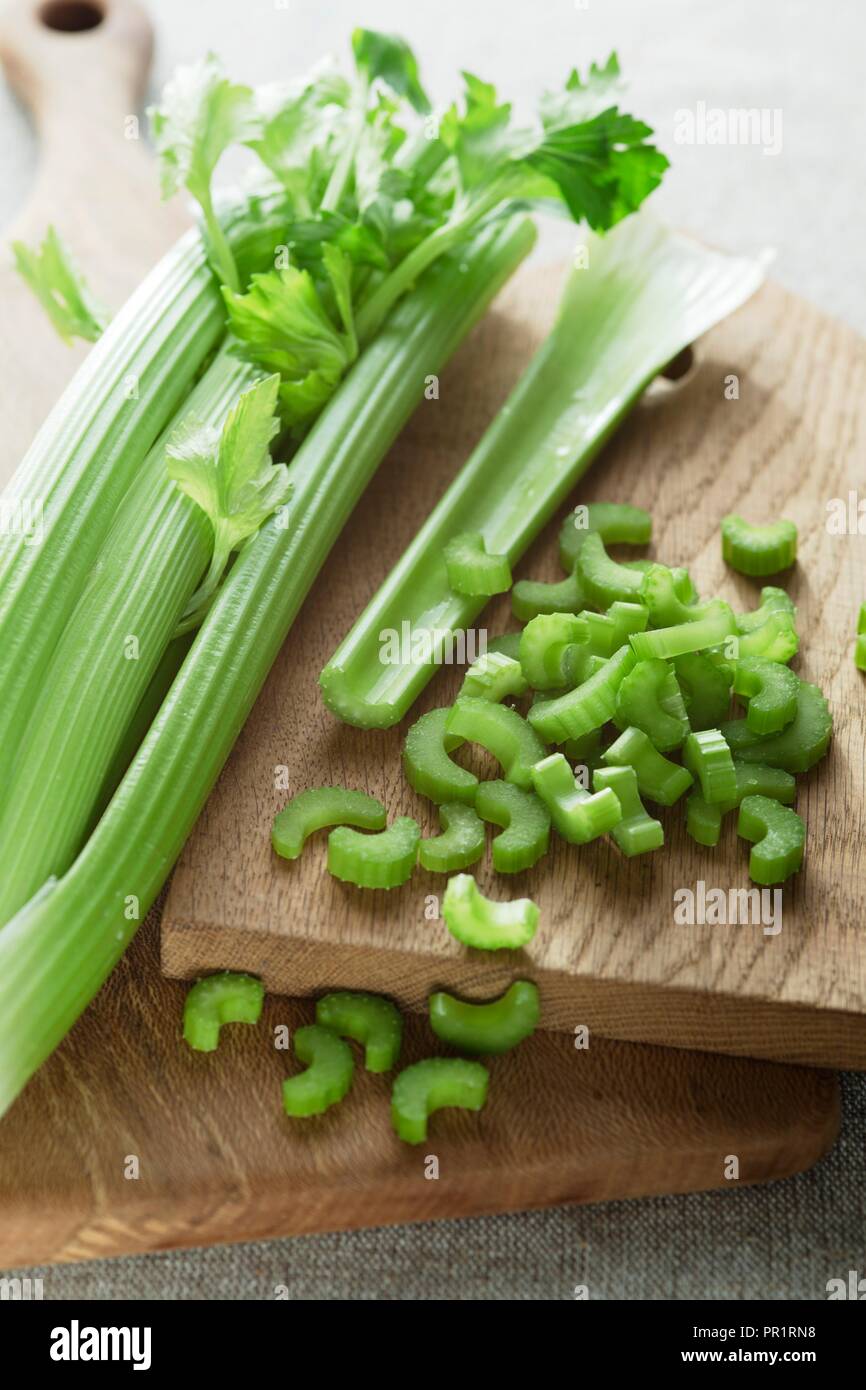 Testa di sedano su un tagliere di legno con fettine di sedano che giace accanto ad essa. Foto Stock