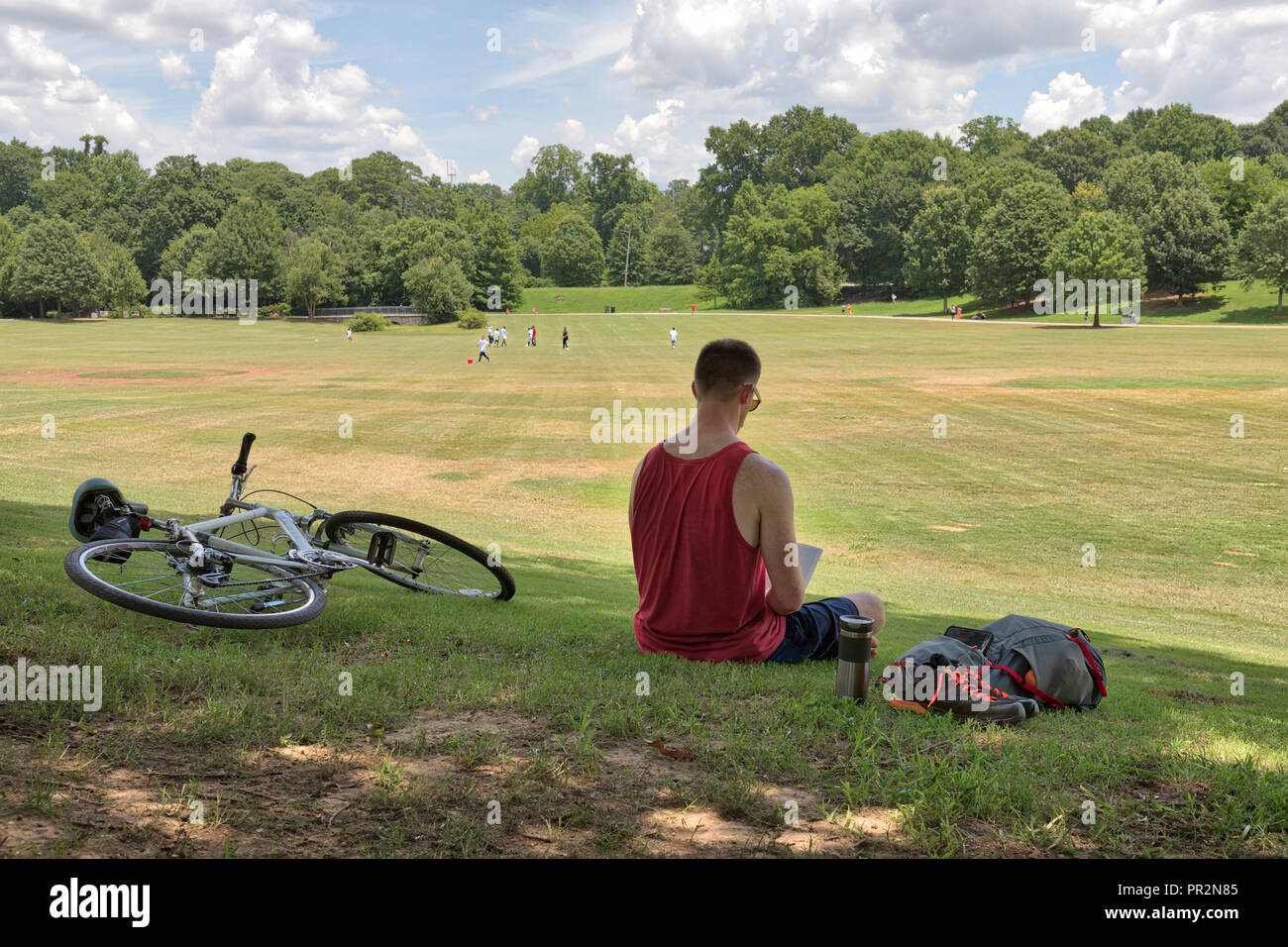 Persona non identificabili la lettura di un libro in Piemonte Park in una giornata di sole con una bici e zaino e altre persone a giocare nella distanza sul verde gr Foto Stock