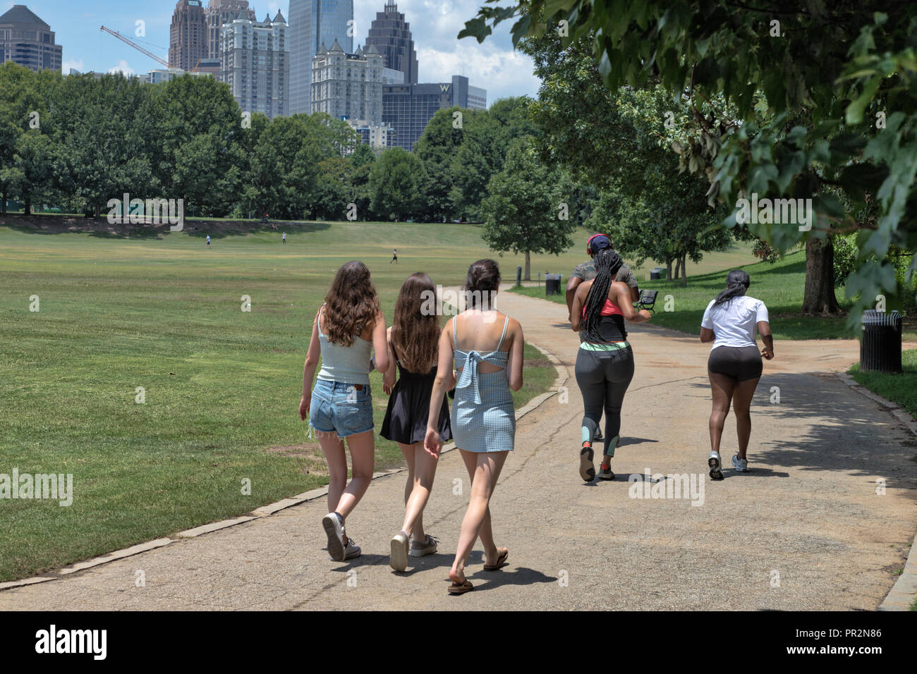 Scuotipaglia non identificabili e guide su un percorso in Piemonte Park di Atlanta, GA in una calda giornata estiva con edifici di distanza Foto Stock