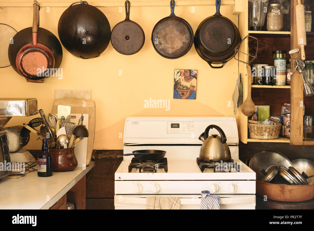 Ghisa pentole appesi sopra una stufa di bianco in una vecchia casa colonica di cucina. Utensili da cucina sono su ogni lato. Foto Stock