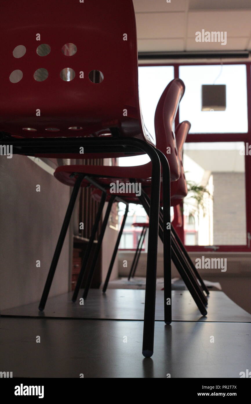 Stampato in rosso le sedie in plastica in piedi su tavoli pieghevoli con una finestra rossa in background e pareti bianche. Foto Stock