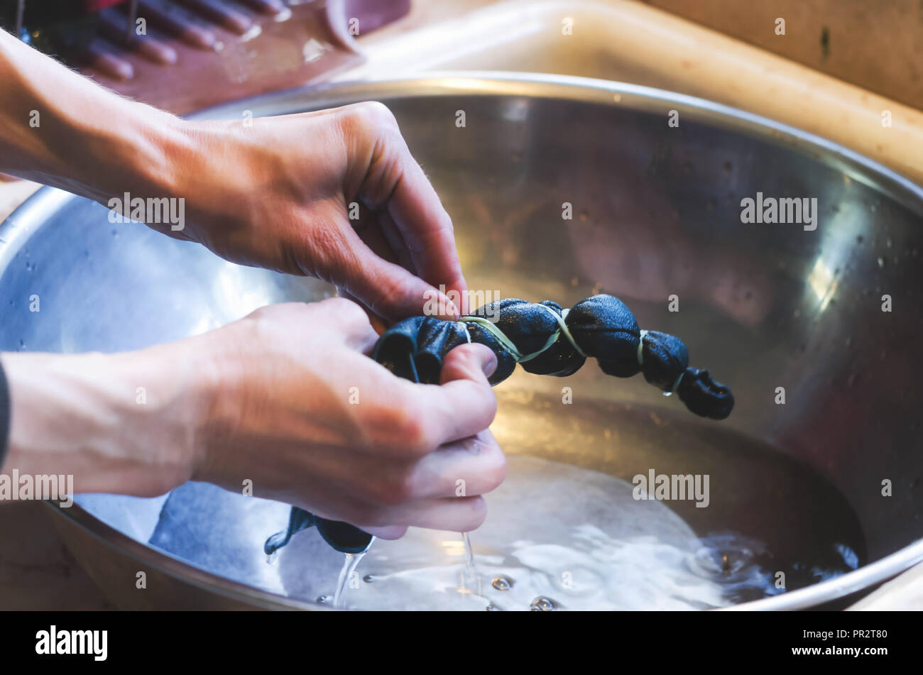 Una donna la rimozione della fascia di gomma da capi di abbigliamento durante il tie-processo di tintura. Rendendo abbigliamento artigianali art. Foto Stock