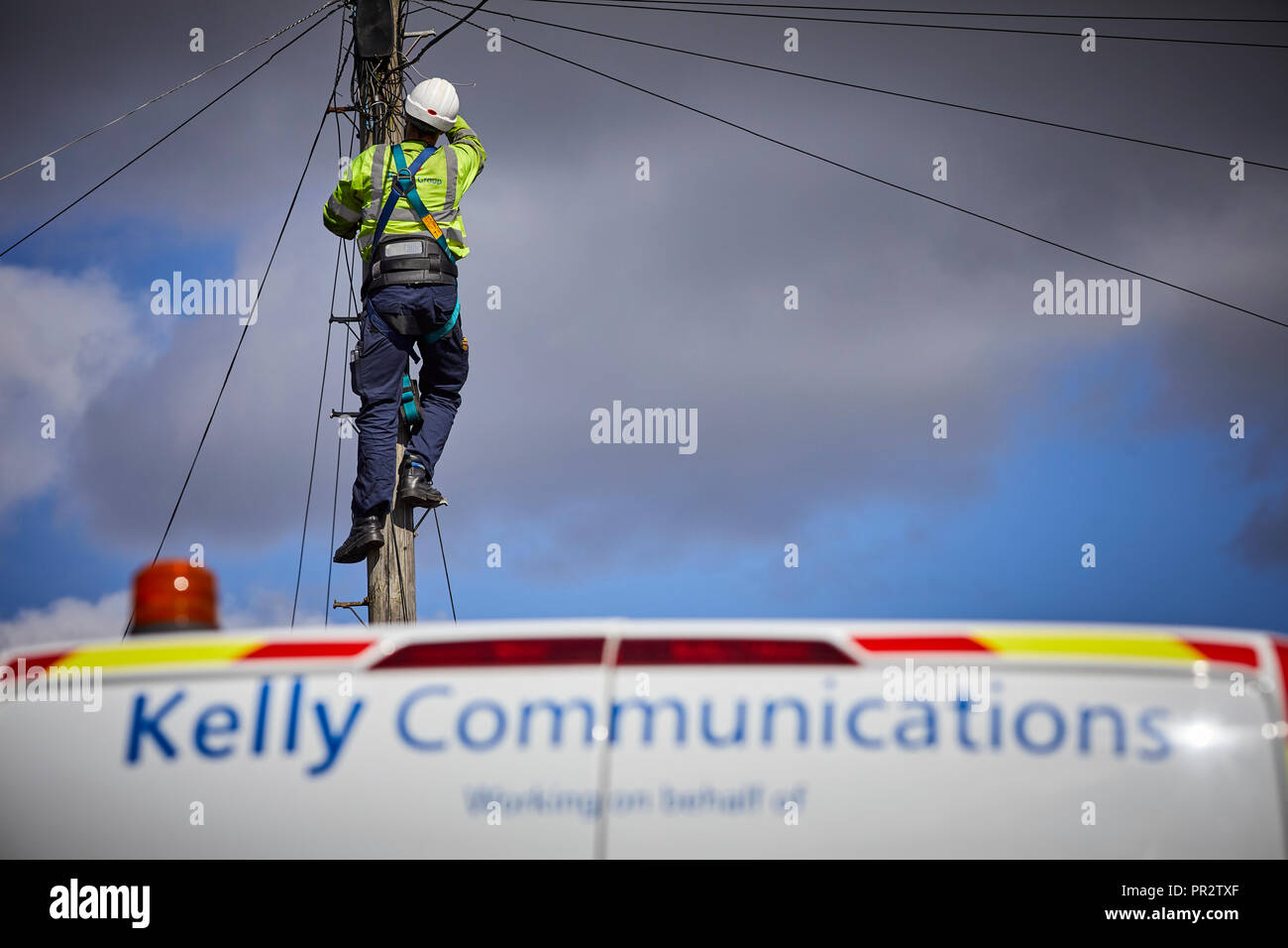 I contraenti telecome ingegnere da Kelly Communications scalata di un palo telefonico per fissare una linea telefonica funzionante subfornitore per BT Openreach in Ma Foto Stock