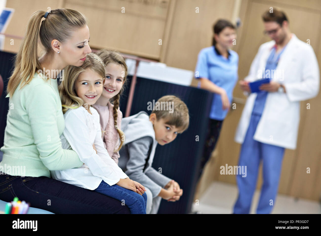 Madre e bambini in attesa nella parte anteriore del banco di registrazione in ospedale Foto Stock