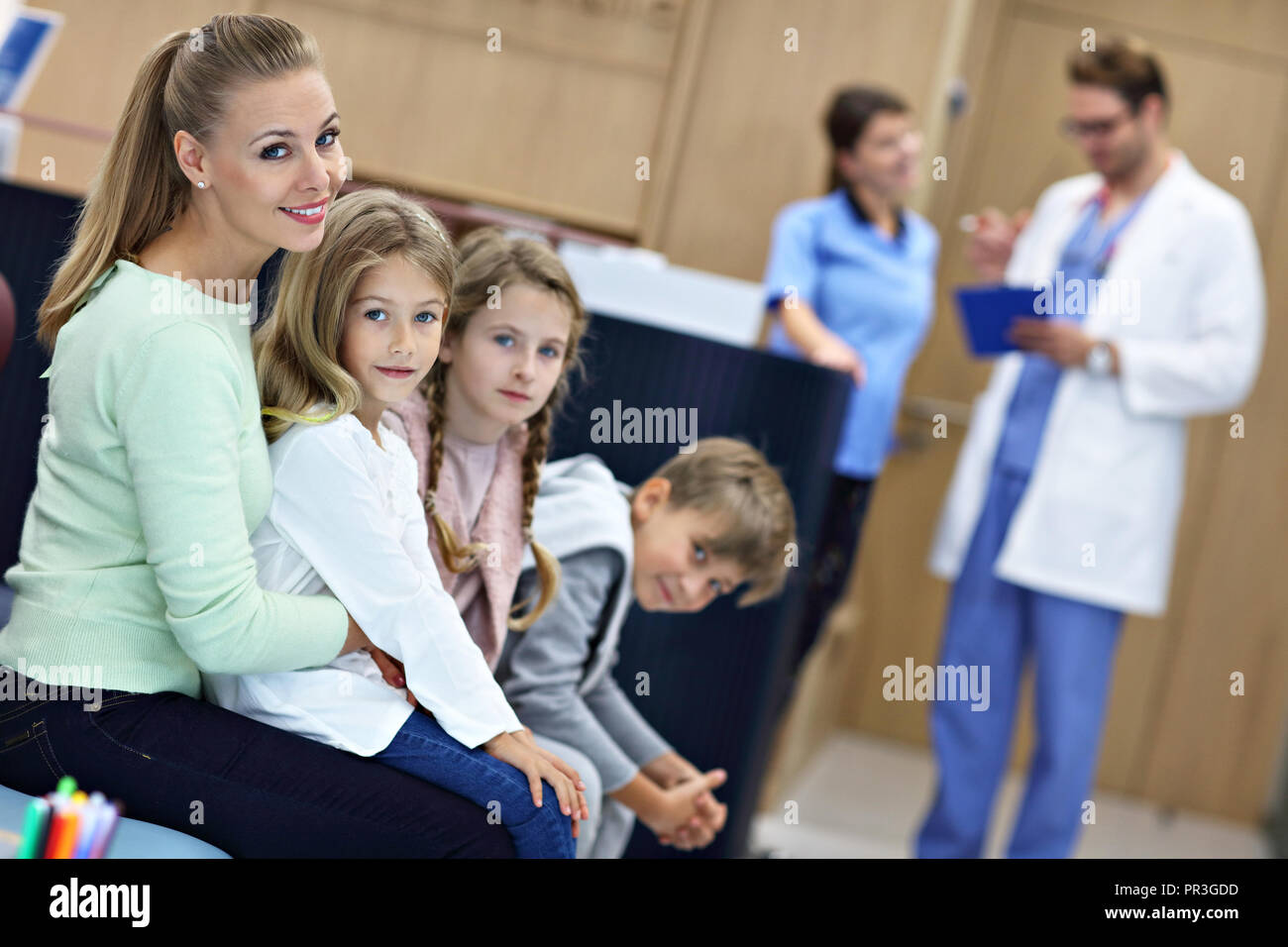 Madre e bambini in attesa nella parte anteriore del banco di registrazione in ospedale Foto Stock