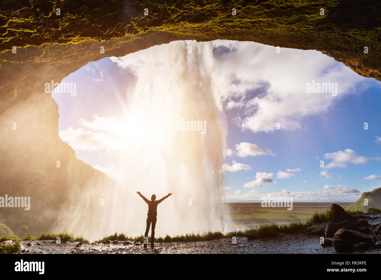 Felice viaggiatori femmina con la sensazione che il potere della cascata Seljalandsfoss nel sud dell'Islanda, della persona in piedi dietro il flusso, la luce del tramonto, intenso Foto Stock