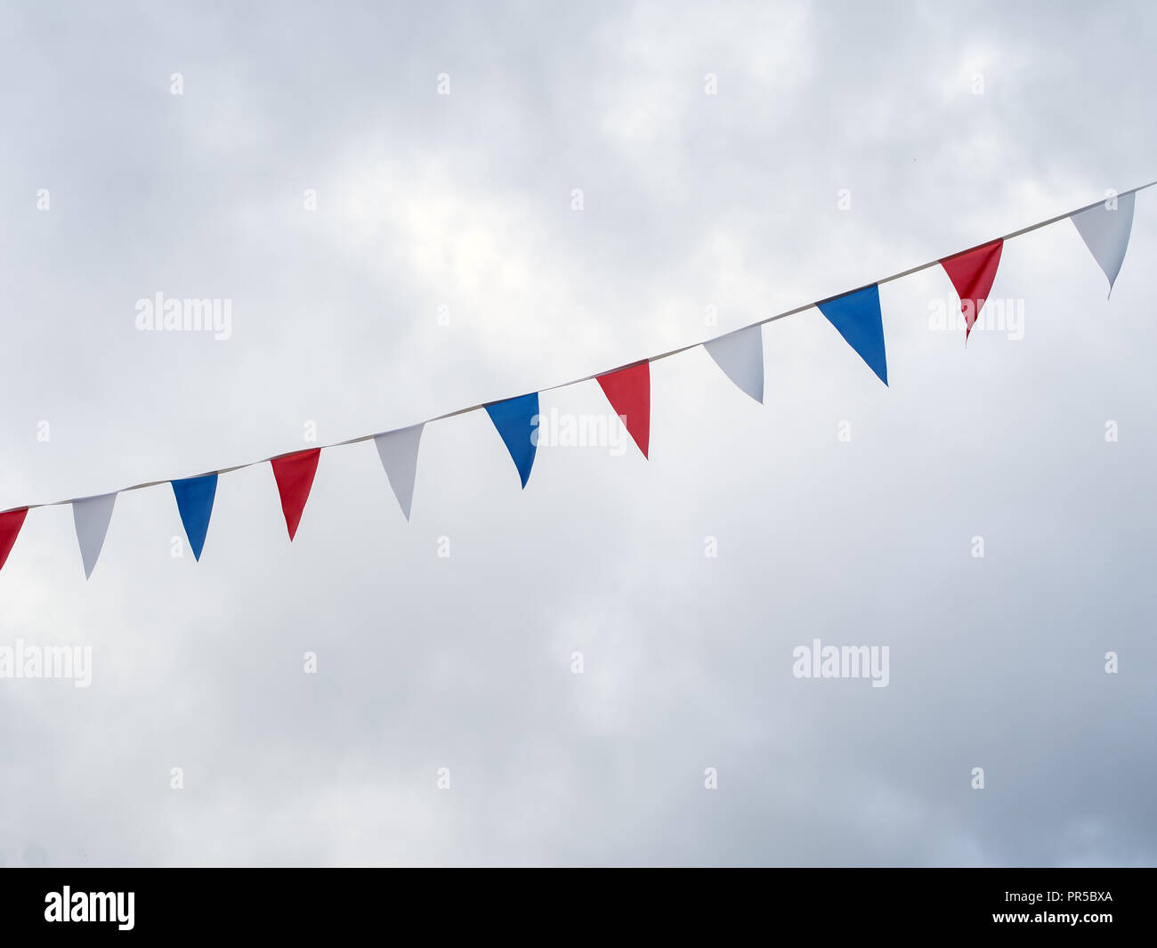 Rosso, bianco e blu festosa bunting bandiere contro lo sfondo del cielo. Forma Triangolare contro il cielo nuvoloso. Foto Stock