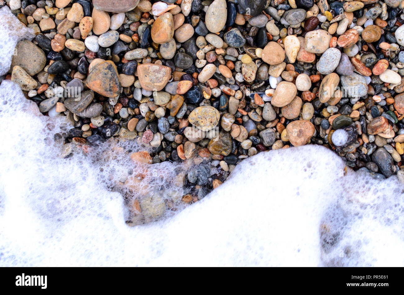 I ciottoli sulla spiaggia con la schiuma delle onde Foto Stock