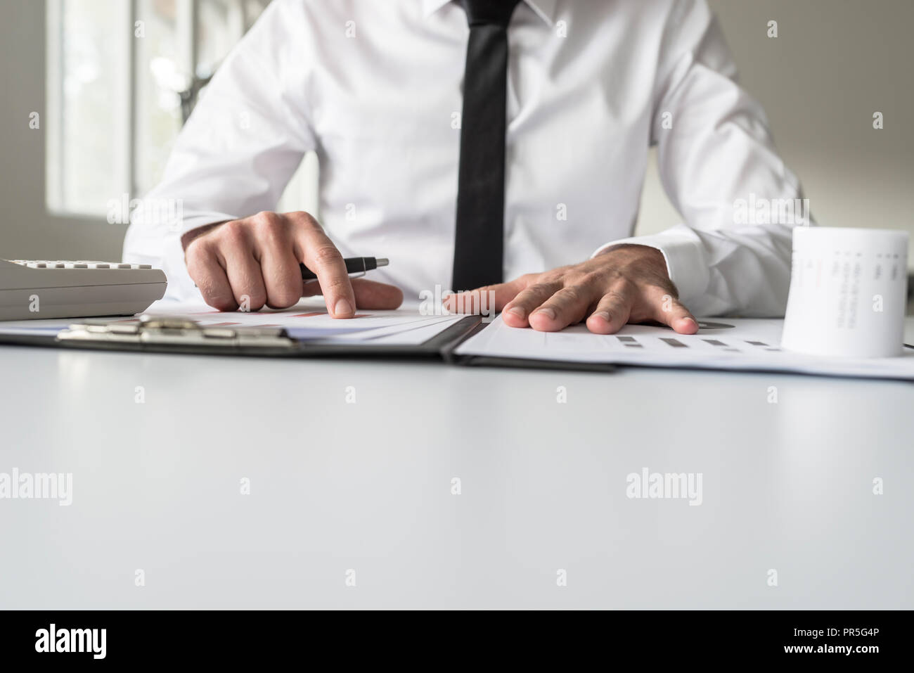 Basso angolo di visione di un imprenditore che puntano a un grafico di analisi su un bianco scrivania in ufficio con il suo dito. Foto Stock