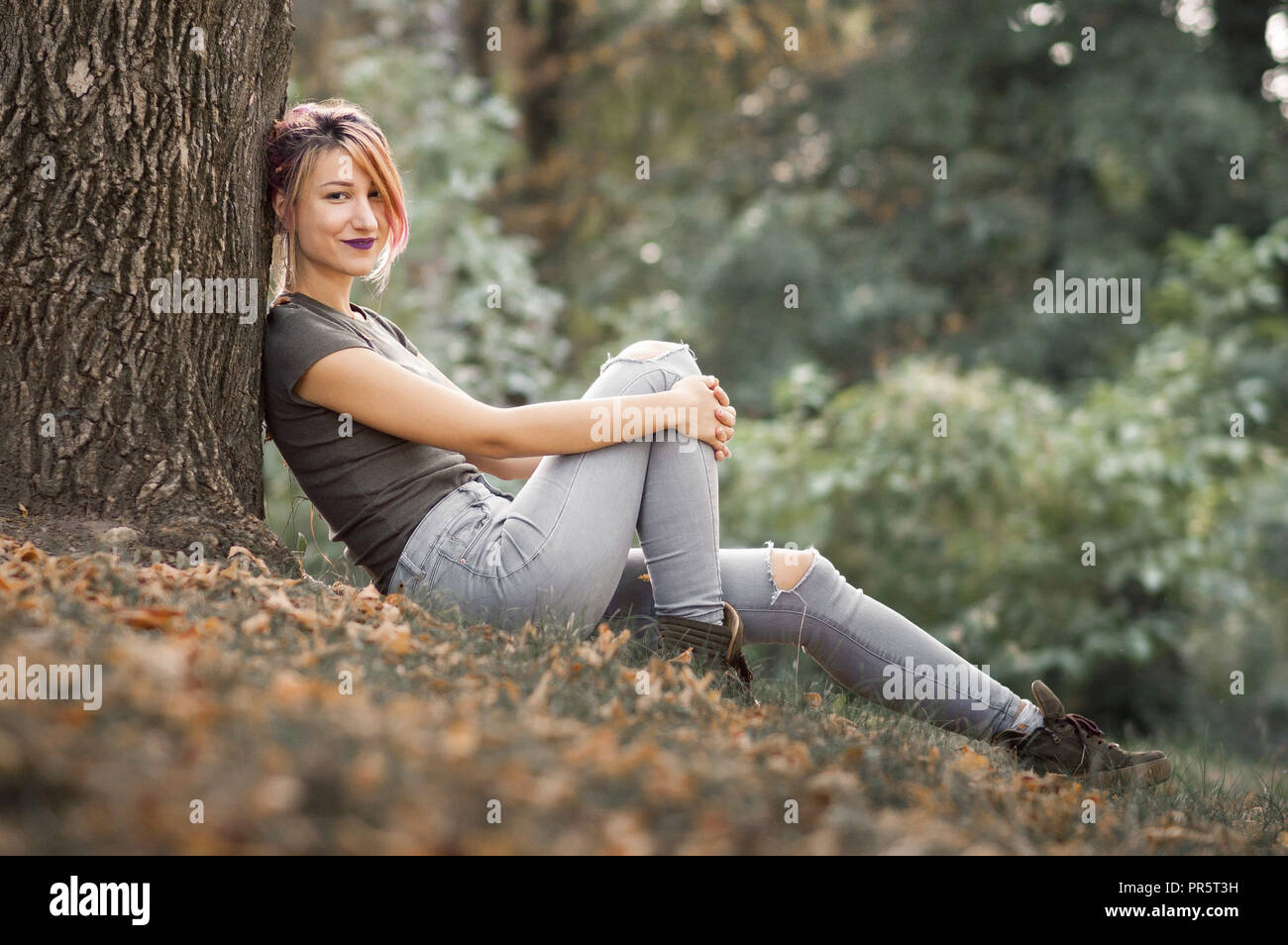 Giovane donna in appoggio mediante una struttura ad albero in posizione di parcheggio Foto Stock