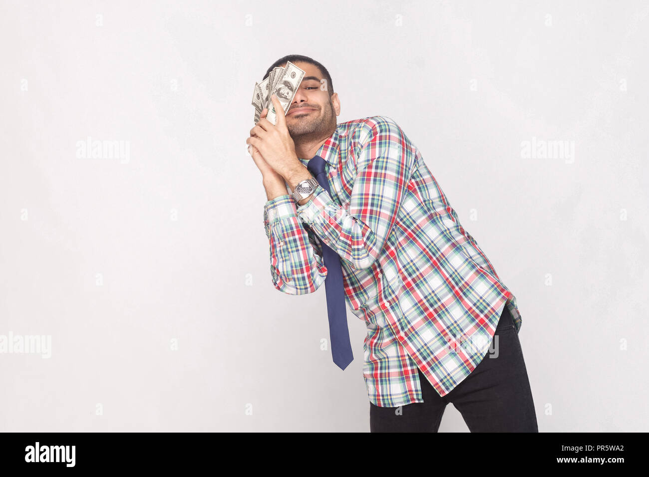 Sogno! Soddisfatto ricco bello barbuto imprenditore in variopinti camicia a scacchi con cravatta blu permanente e la magra contro a guancia fan di denaro Foto Stock