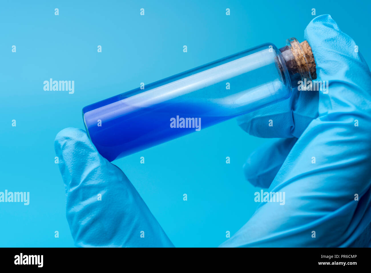 Close-up di tubo di vetro con fluido blu in mano dello scienziato durante il test medici. Una mano tiene un pallone di liquido di colore blu. Foto Stock