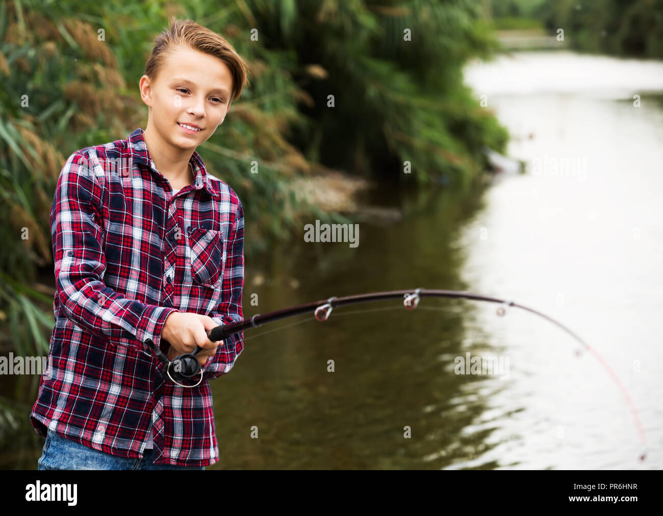 Allegro ragazzo adolescente di pesca sul lago d'acqua dolce dalla riva Foto Stock