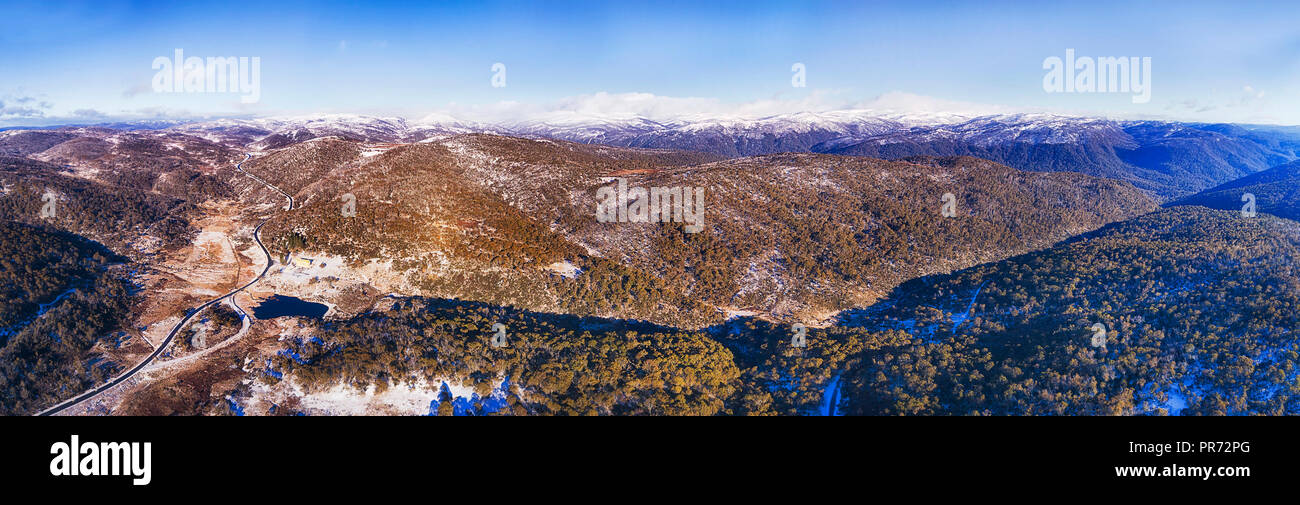 Escavatrice creek in alta montagna innevata in inverno con il bianco della neve il coperchio sul terreno freddo e distante picchi di Kosciusko national park in antenna elevata p Foto Stock